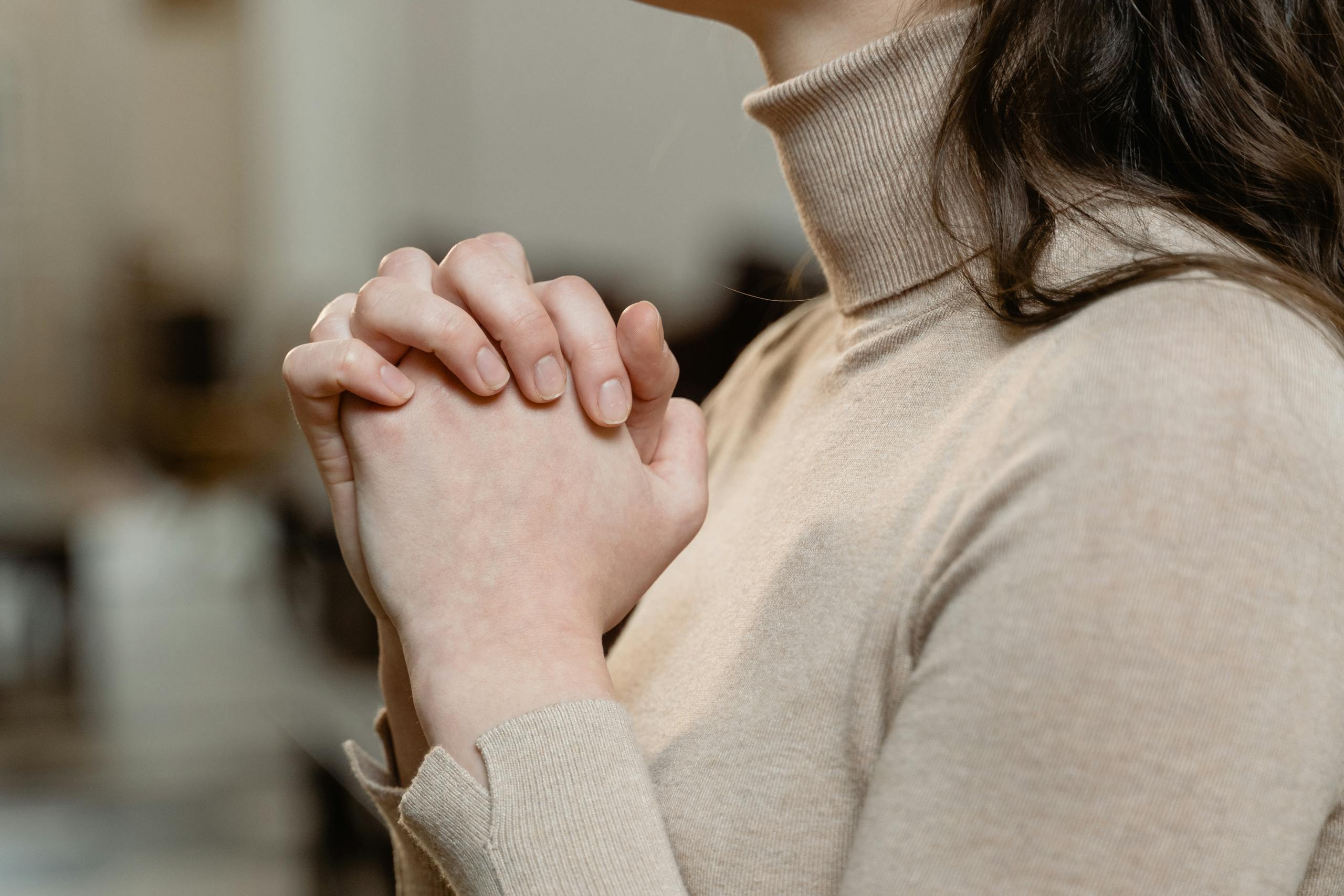 A woman in a turtleneck prays with clasped hands, symbolizing faith and spirituality.