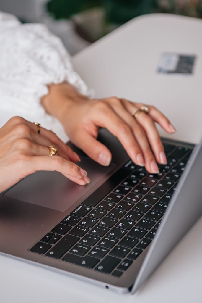 Hands of a woman typing on a laptop keyboard indoors, showcasing rings and fashion.