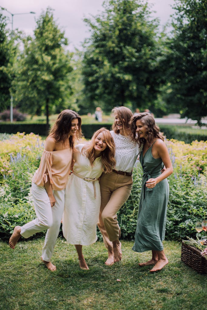 Group of four happy women laughing and embracing outdoors in a lush park setting.
